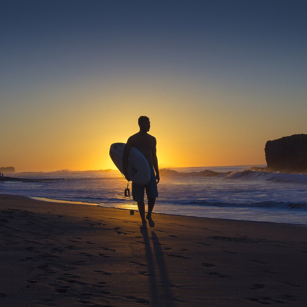 A surfer walking the beach at sunset